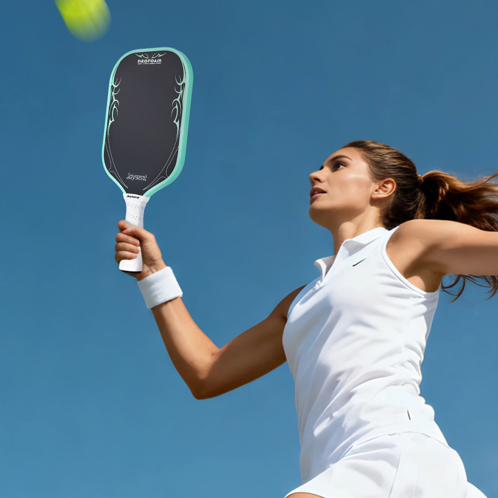 Woman playing pickleball with a paddle against a clear blue sky